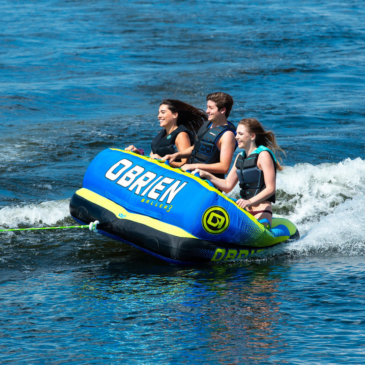 Three riders on an OBrien Baller 3 being towed over waves.