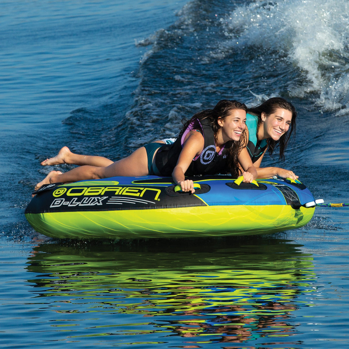 Two people smiling while riding waves on an OBrien D-Lux 2 Towable Tube.