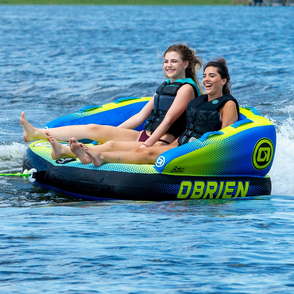Two people smile while riding the OBrien Baller 2 Towable Tube on a lake adventure.