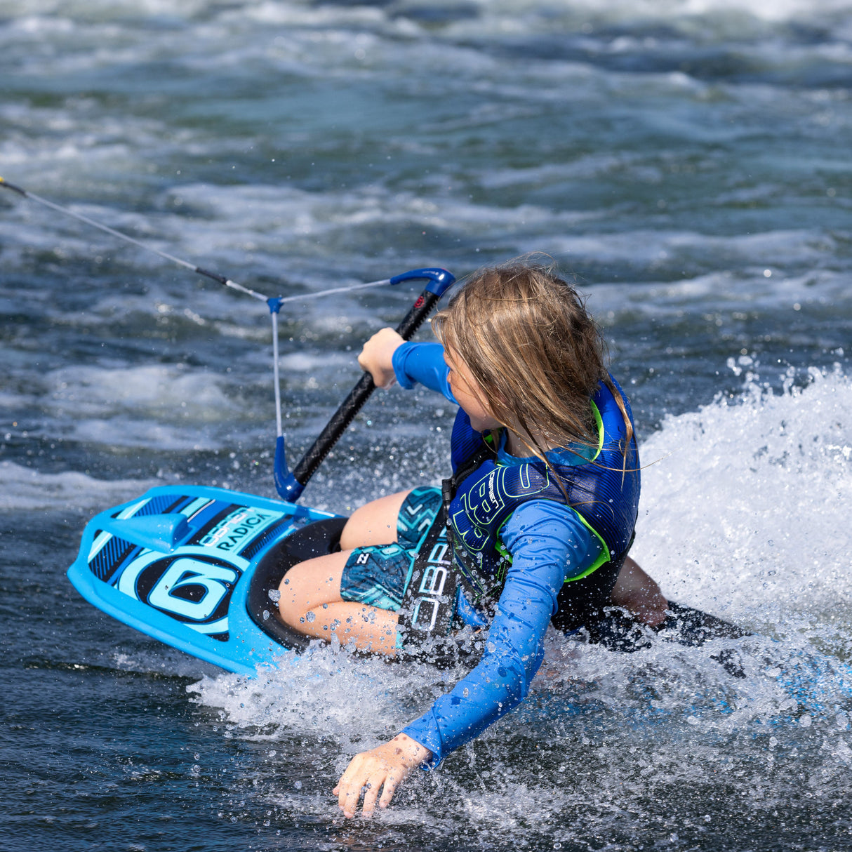 Rear view of a young rider kneeboarding on the O'Brien Radica, turning through the wake while holding onto the tow handle.