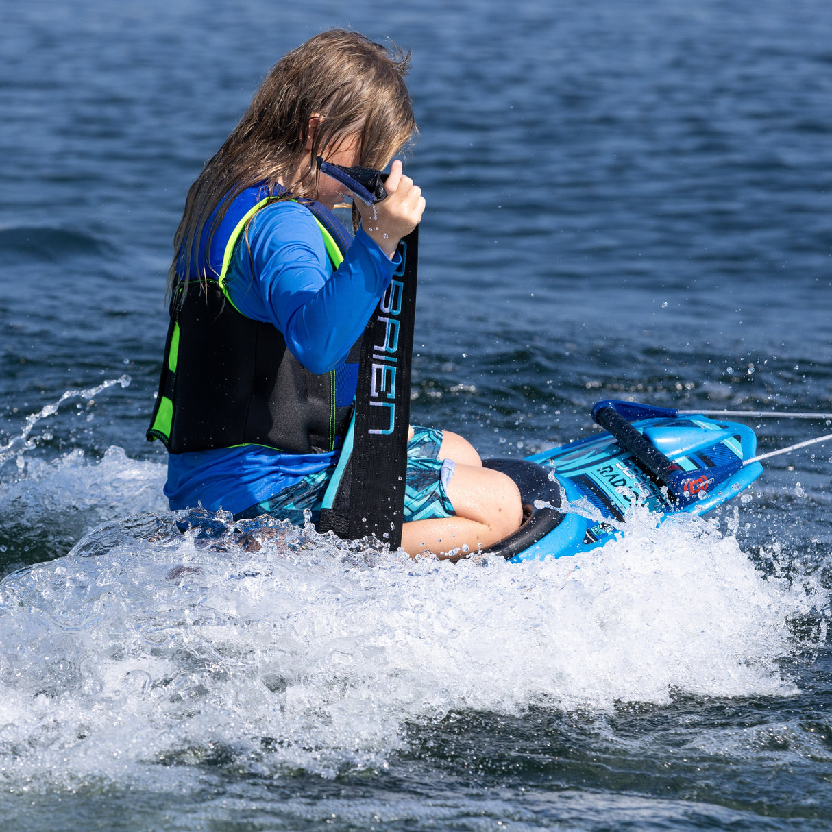 A young rider on the O'Brien Radica sits back, adjusting the padded strap while floating in the water.