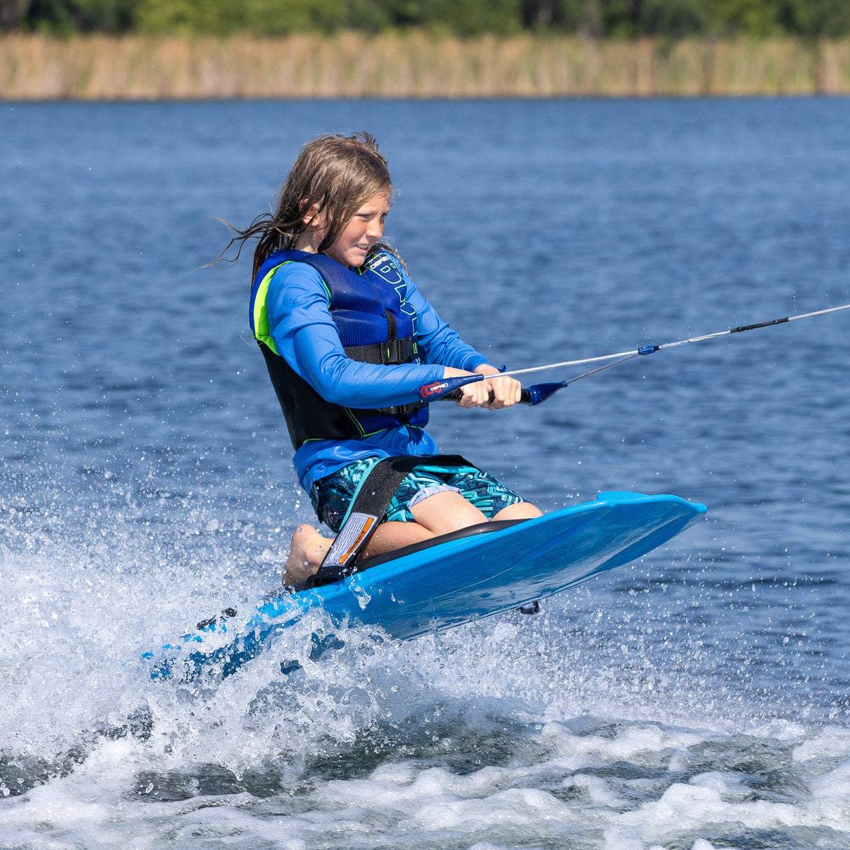 A young rider kneeboarding on the O'Brien Radica leans back while gripping the handle, kicking up a small wake.
