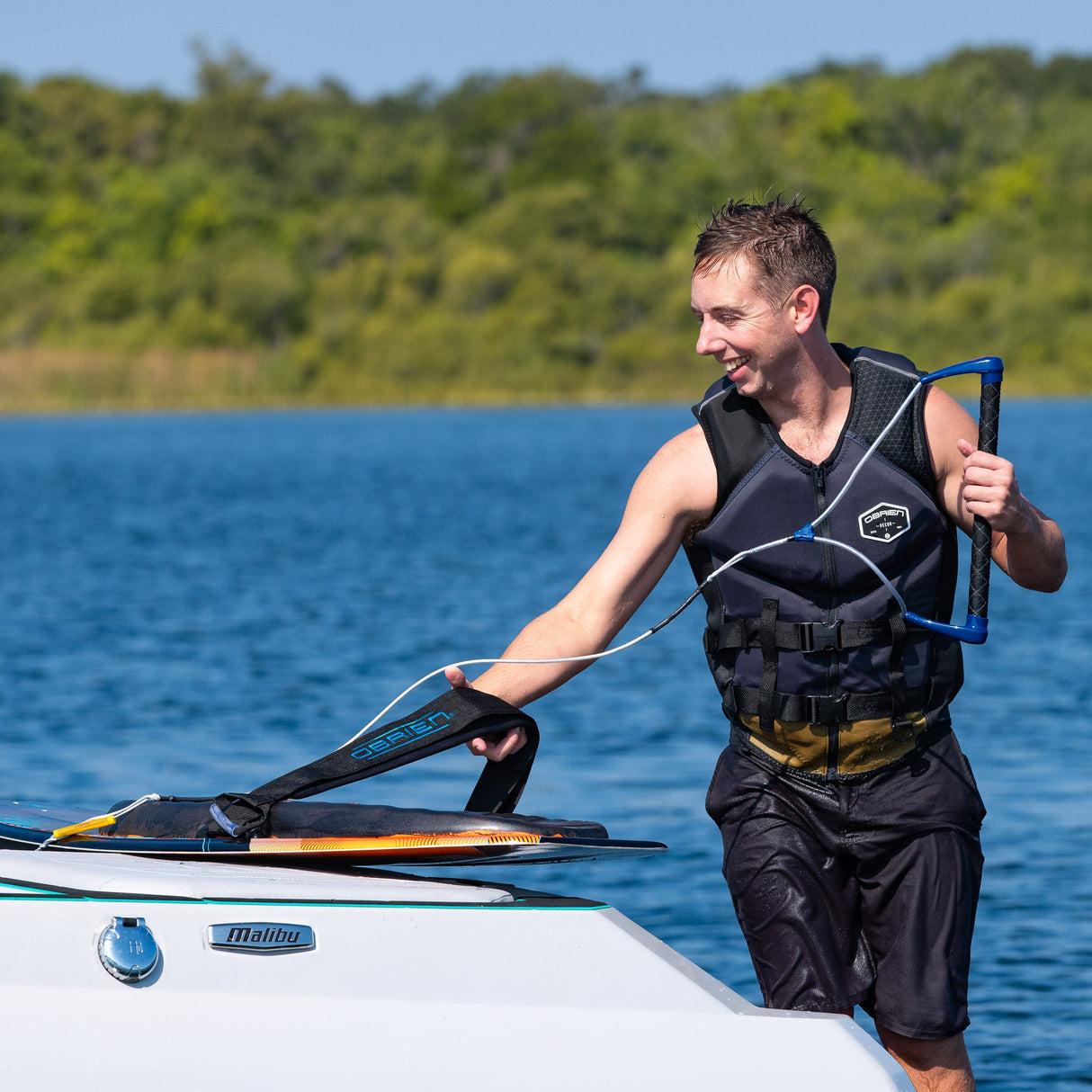A rider in a black life jacket places the Ricochet Kneeboard on a boat while holding onto a tow rope.