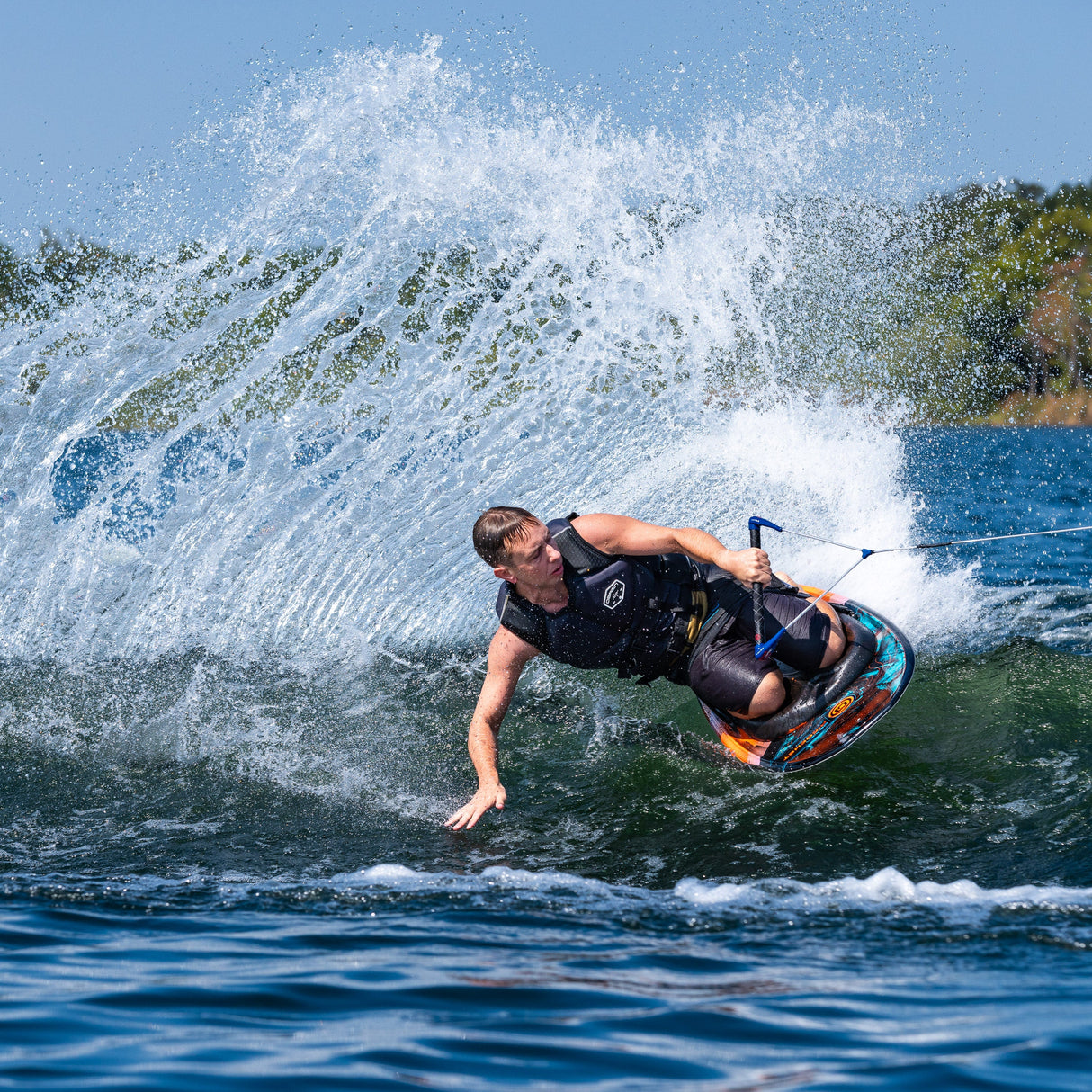 A rider carves through the water on the Ricochet Kneeboard, creating a large spray of water behind them.