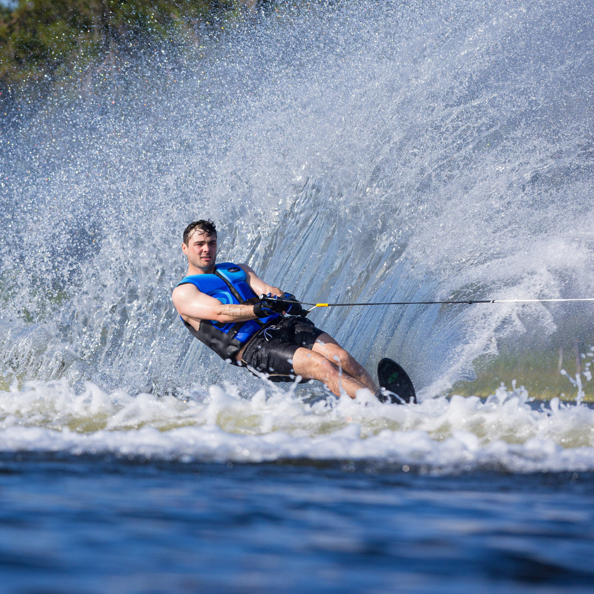 Skier carving on the O'Brien Siege Slalom Waterski, creating a spray while wearing a blue vest.