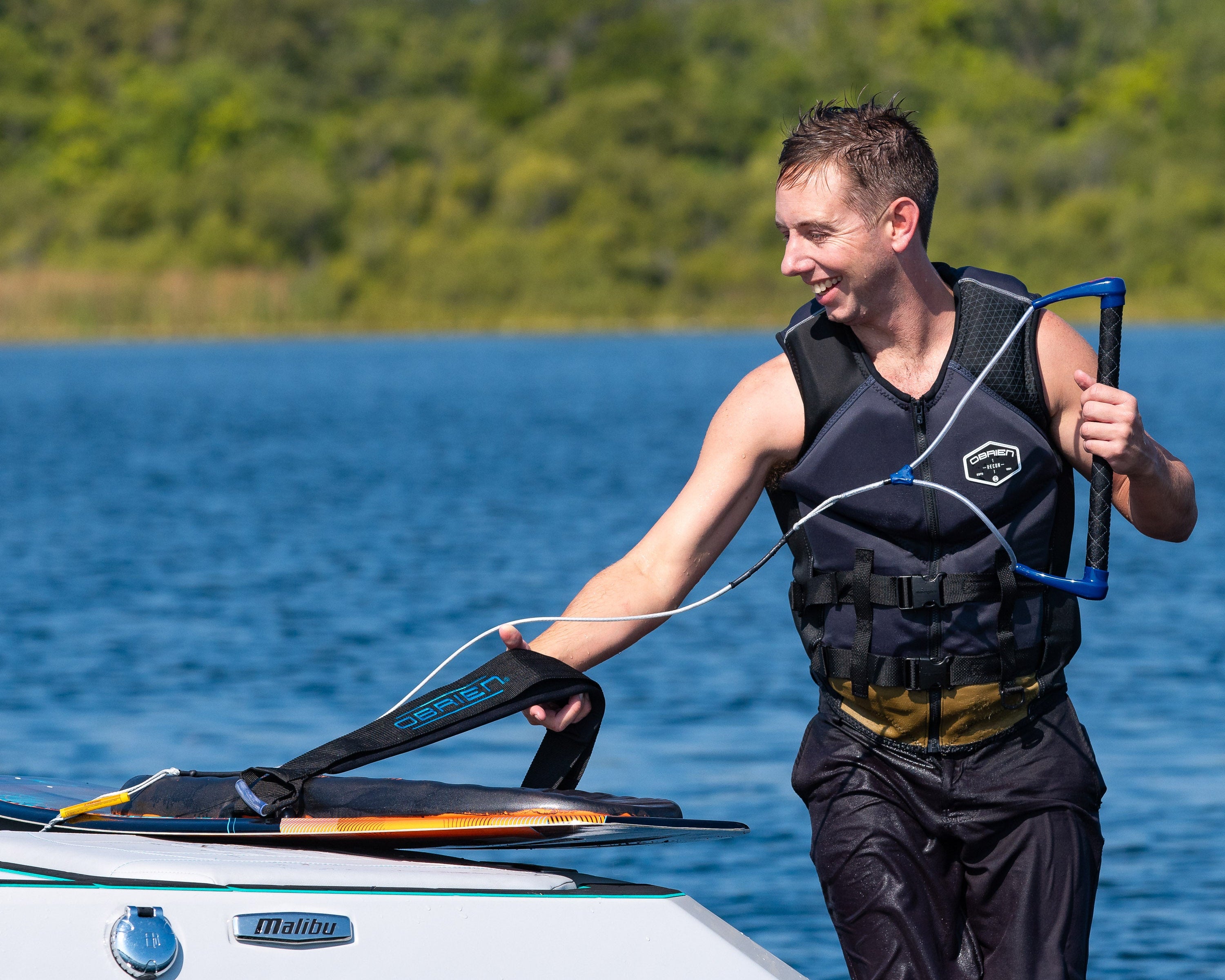 A rider in a black life jacket places the Ricochet Kneeboard on a boat while holding onto a tow rope.