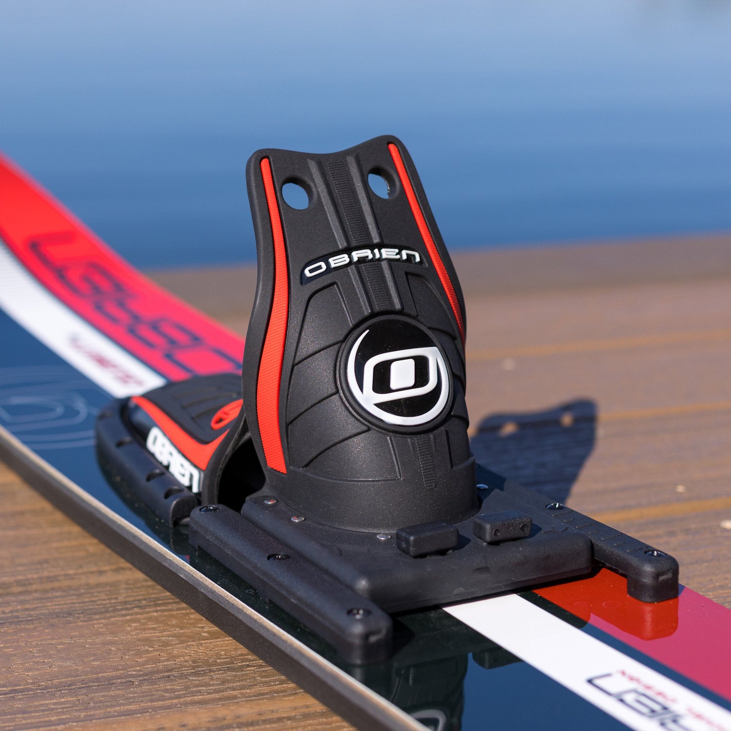 Close-up of a black ski binding on a red and white ski with a blurred blue background