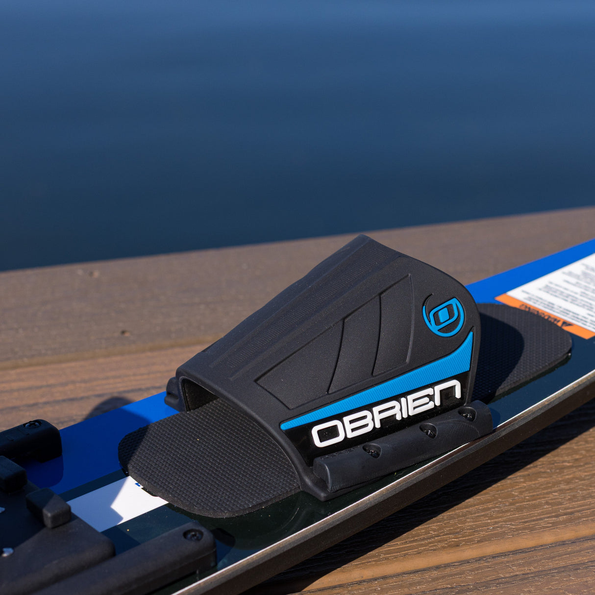 Close-up of a black and blue O'Brien ski boot binding on a ski with a blurred water background